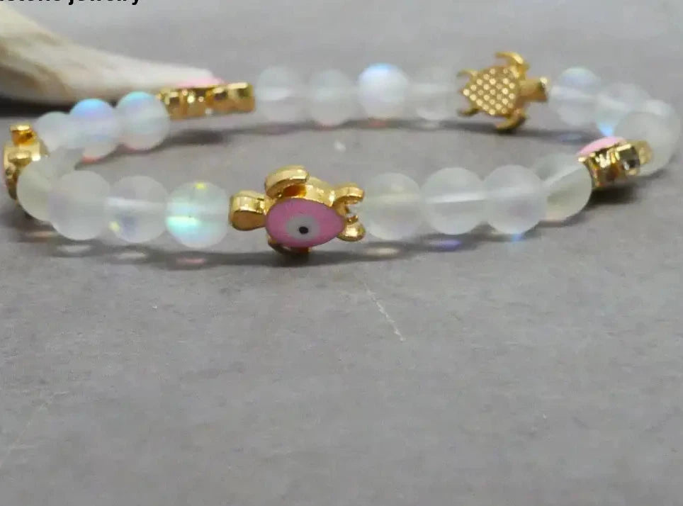 Beaded bracelet with gold accents and a pink charm on a gray surface