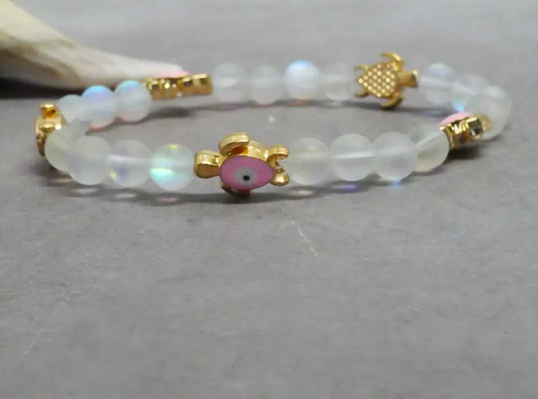 Beaded bracelet with gold accents and a pink charm on a gray surface